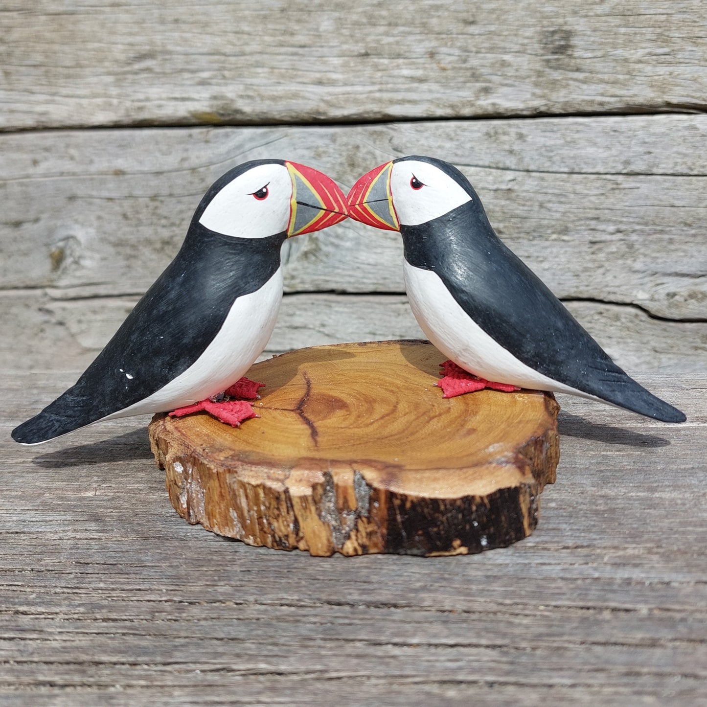 Two hand made wooden puffin figurines on a wooden base against a wooden background