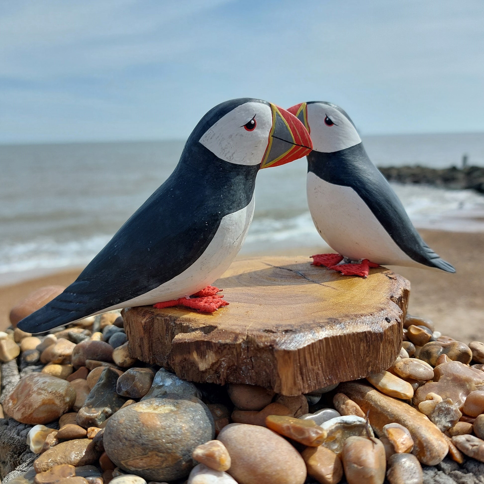 Two puffin figurines handmade in Bali on a wooden platform with a beach background