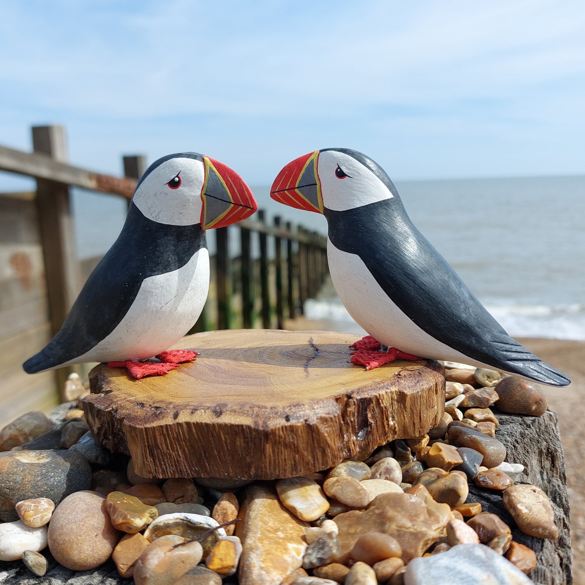 Two wooden puffin figurines on a wooden base with a beach background