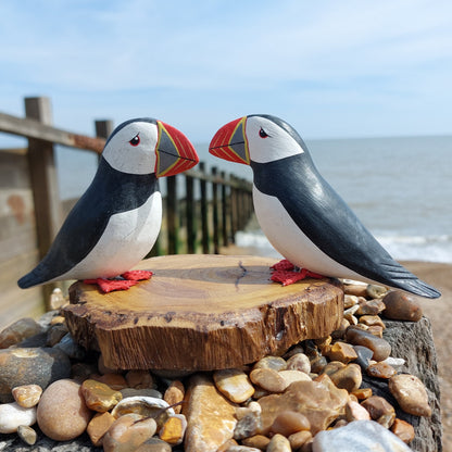 Two wooden puffin figurines on a wooden base with a beach background