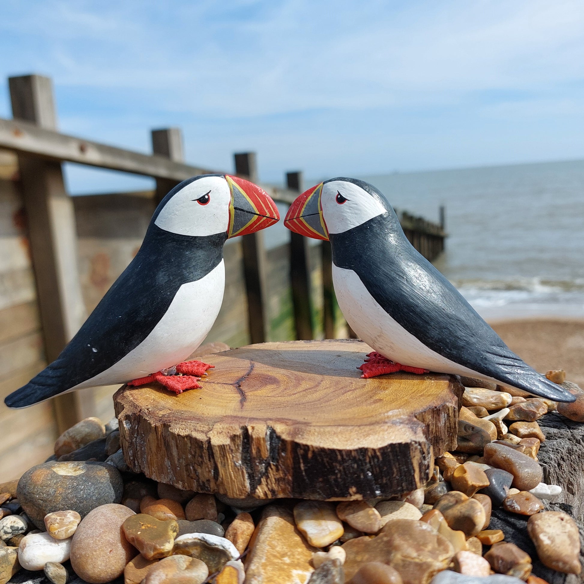 Two wooden handmade puffin statues on a wooden stump by the sea.