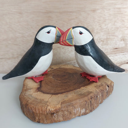 A handmade and painted set of 2 cute puffins mounted on a wood slice against a pale background