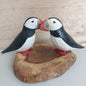 A handmade and painted set of 2 cute puffins mounted on a wood slice against a pale background
