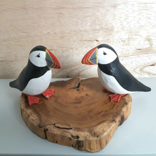 Two puffin figurines on a wooden base against a light wood panel background
