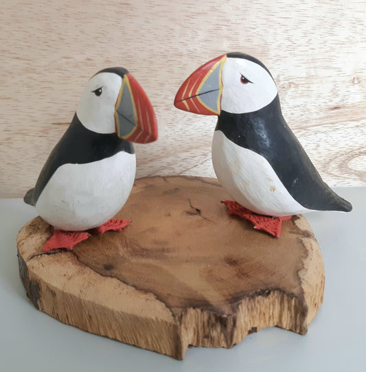 An ornament of 2 wooden carved puffins on a wooden base with a wooden background