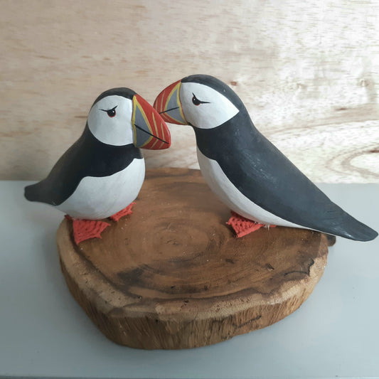 Two puffin figurines on a wooden base against a light wood background