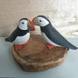 Two puffin figurines on a wooden base against a light wood background