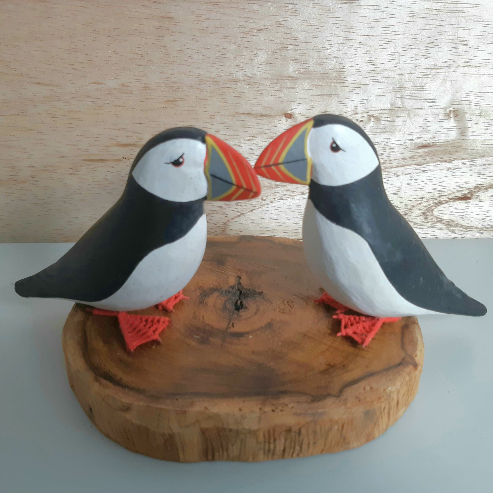 Two puffin figurines on a wooden base against a wooden background