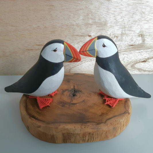 Two puffin figurines on a wooden base against a wooden background