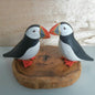 Two puffin figurines on a wooden base against a wooden background