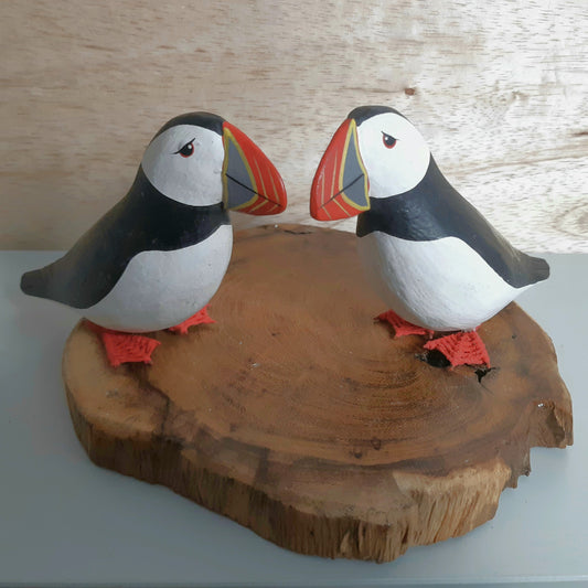 Two puffin figurines on a wooden base against a light wood panel background