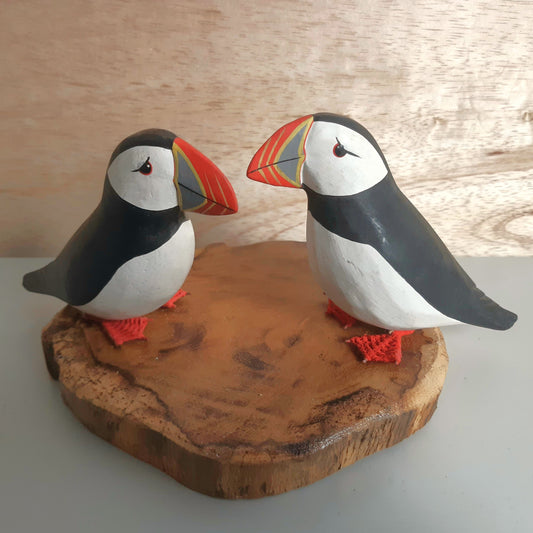 Two puffin figurines on a wooden base with a light wood background