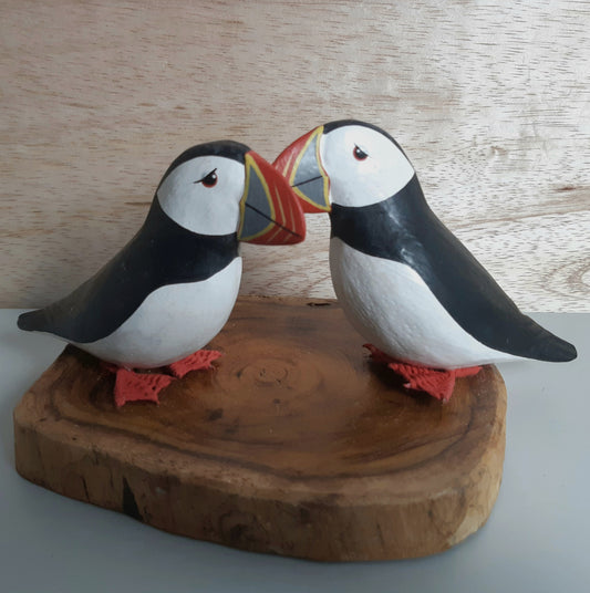 Two puffin figurines on a wooden base with a light wood background
