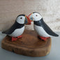 Two puffin figurines on a wooden base with a light wood background