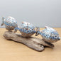 Three carved wooden fish with mosaic patterns on a piece of driftwood against a neutral background