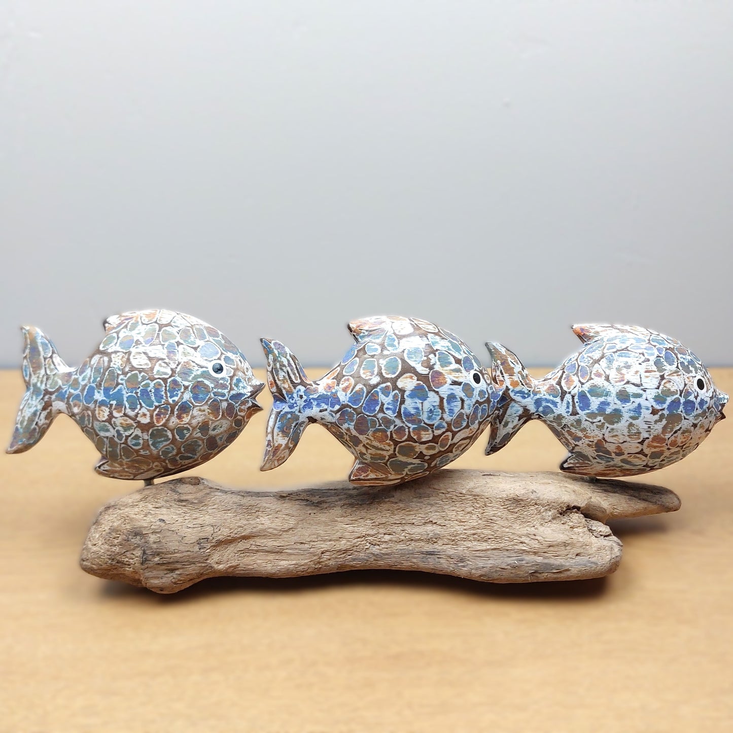 Decorative hand carved and painted fish sculpture on a piece of driftwood with a neutral background