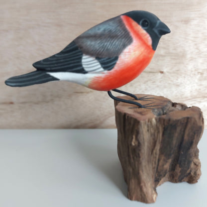 Decorative hand carved and painted Bullfinch bird figurine on a wooden stump against a neutral background