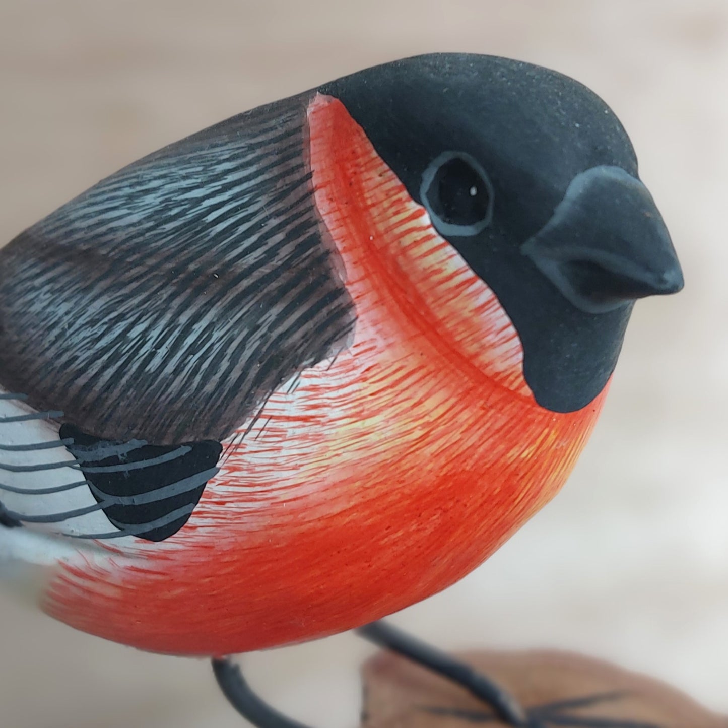 Close-up of a hand painted Bullfinch bird figurine with a red breast and black head.