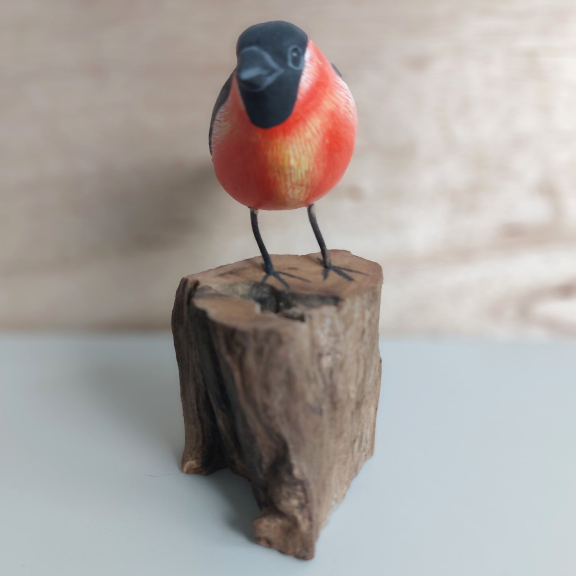 A wooden handmade and painted Bullfinch Bird figurine on a wooden block with a blurred background