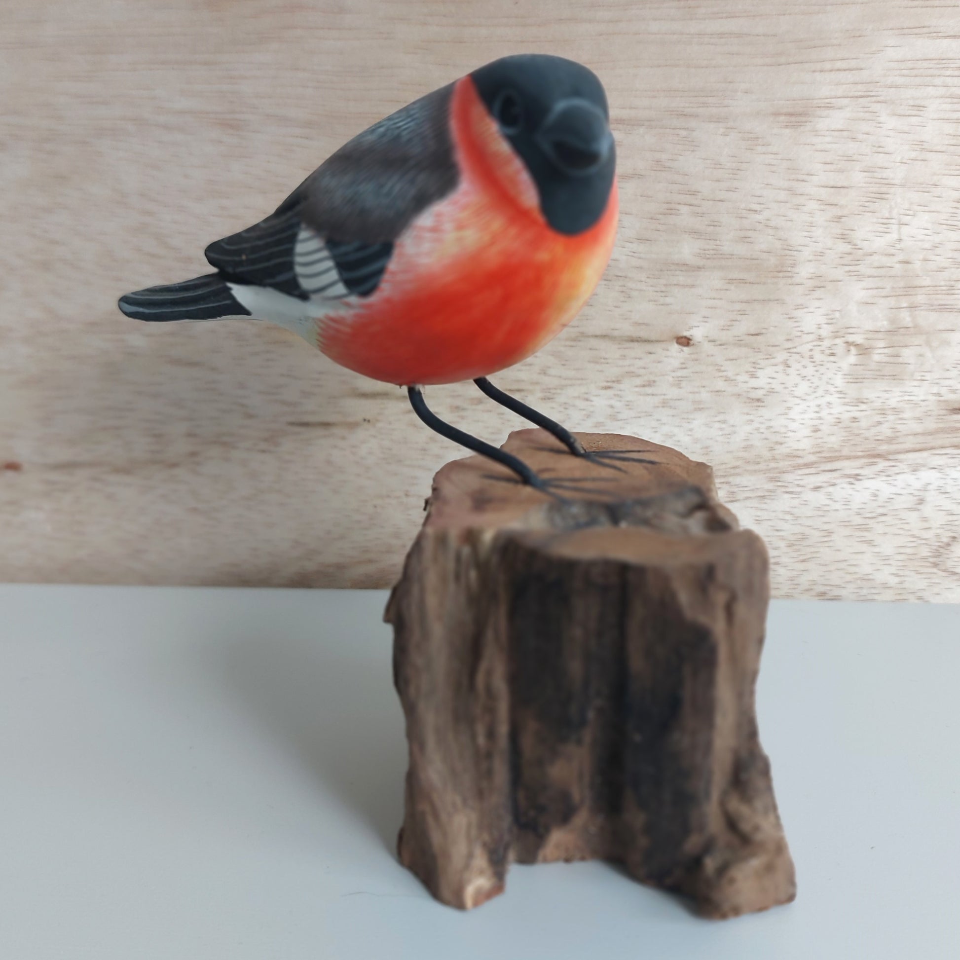 Wooden Ornament of a bullfinch bird perched on a wooden stump against a wooden background