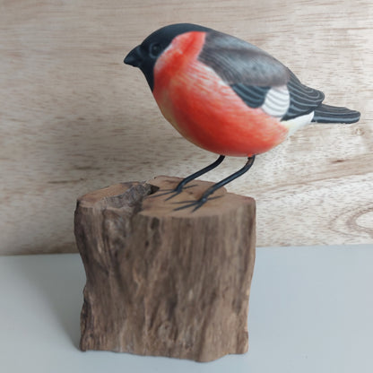 Wooden Bullfinch Bird figurine with red breast and black head perched on a wooden block against a wooden background