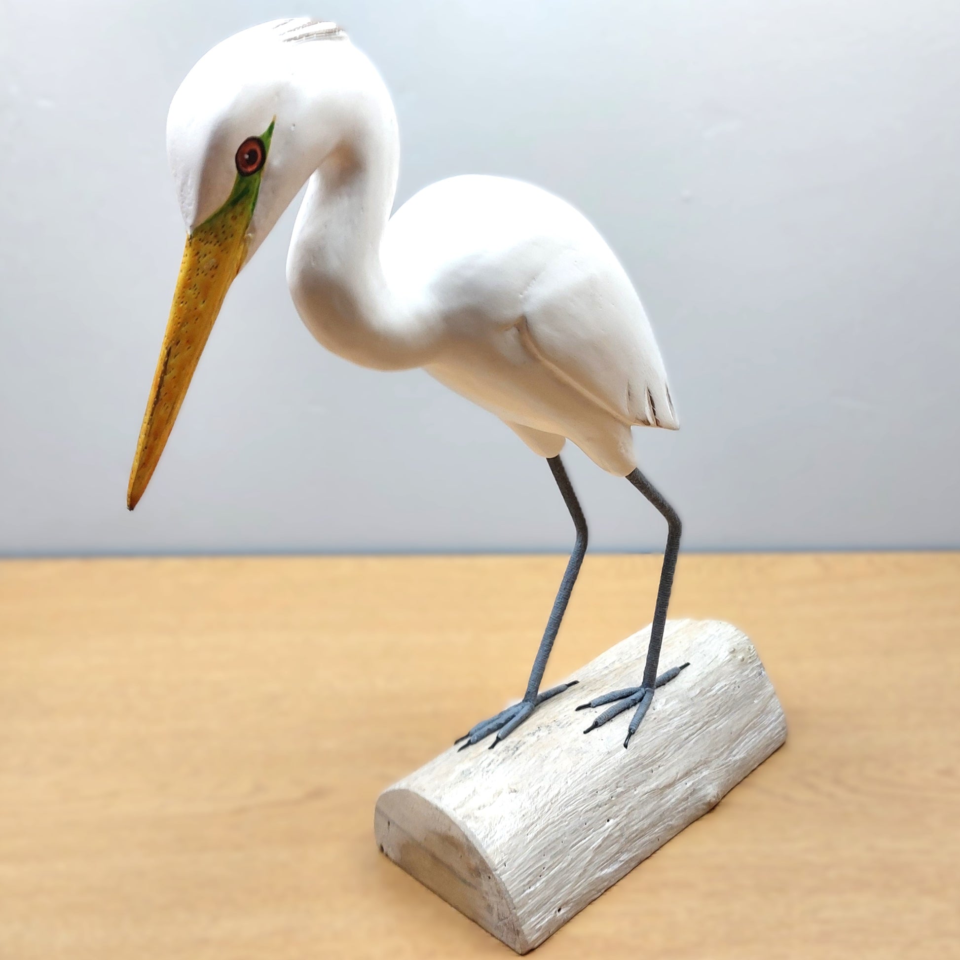 White handmade and carved Egret bird figurine with a yellow beak on a wooden base against a light gray background