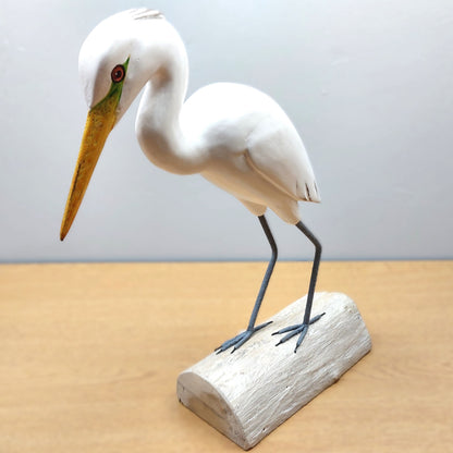 White handmade and carved Egret bird figurine with a yellow beak on a wooden base against a light gray background