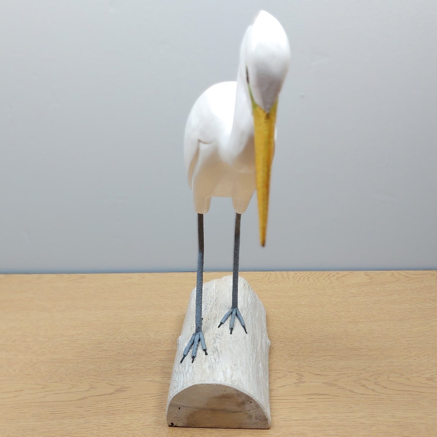 White Egret bird figurine with a yellow beak on a wooden base made in Bali against a gray background