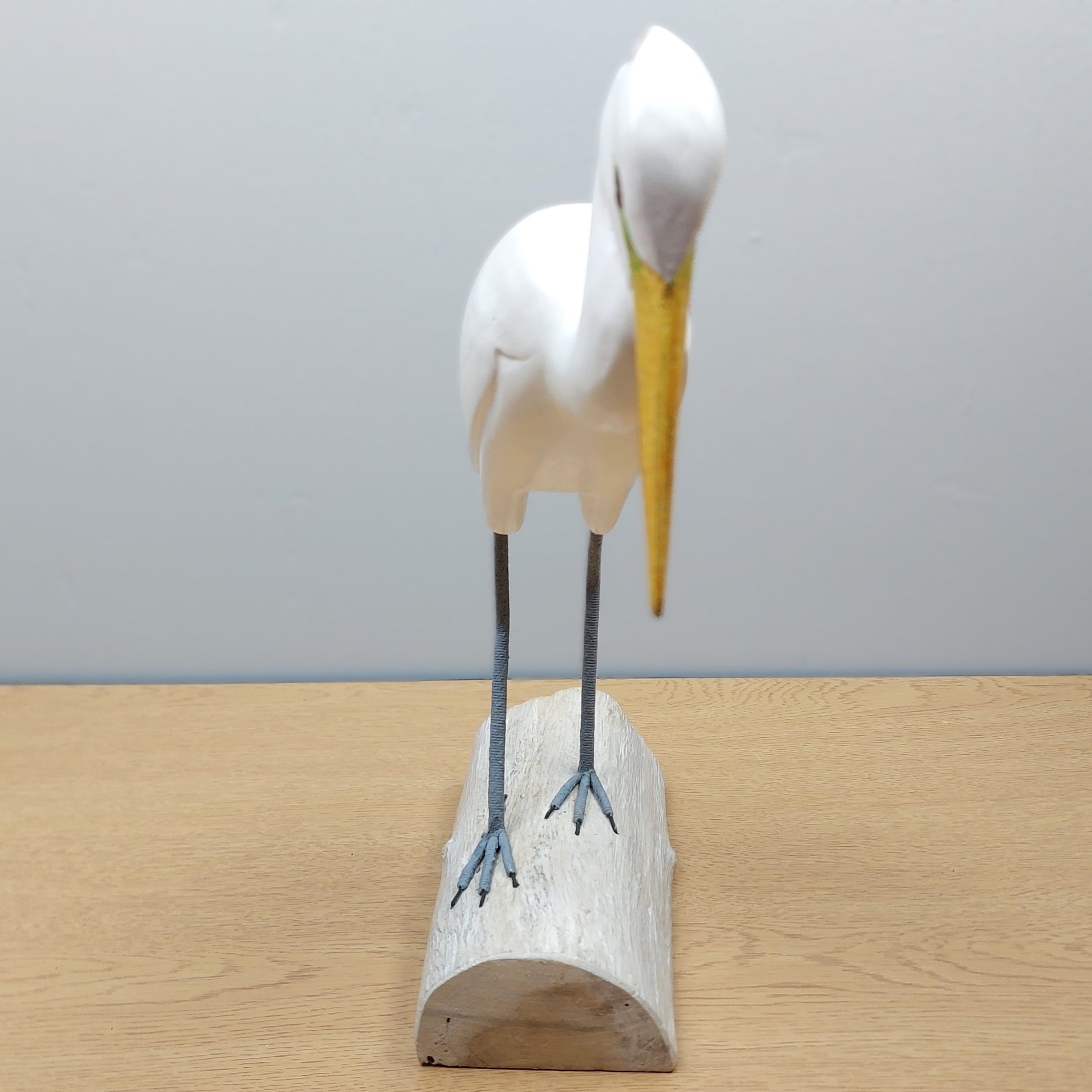 White Egret bird figurine with a yellow beak on a wooden base made in Bali against a gray background