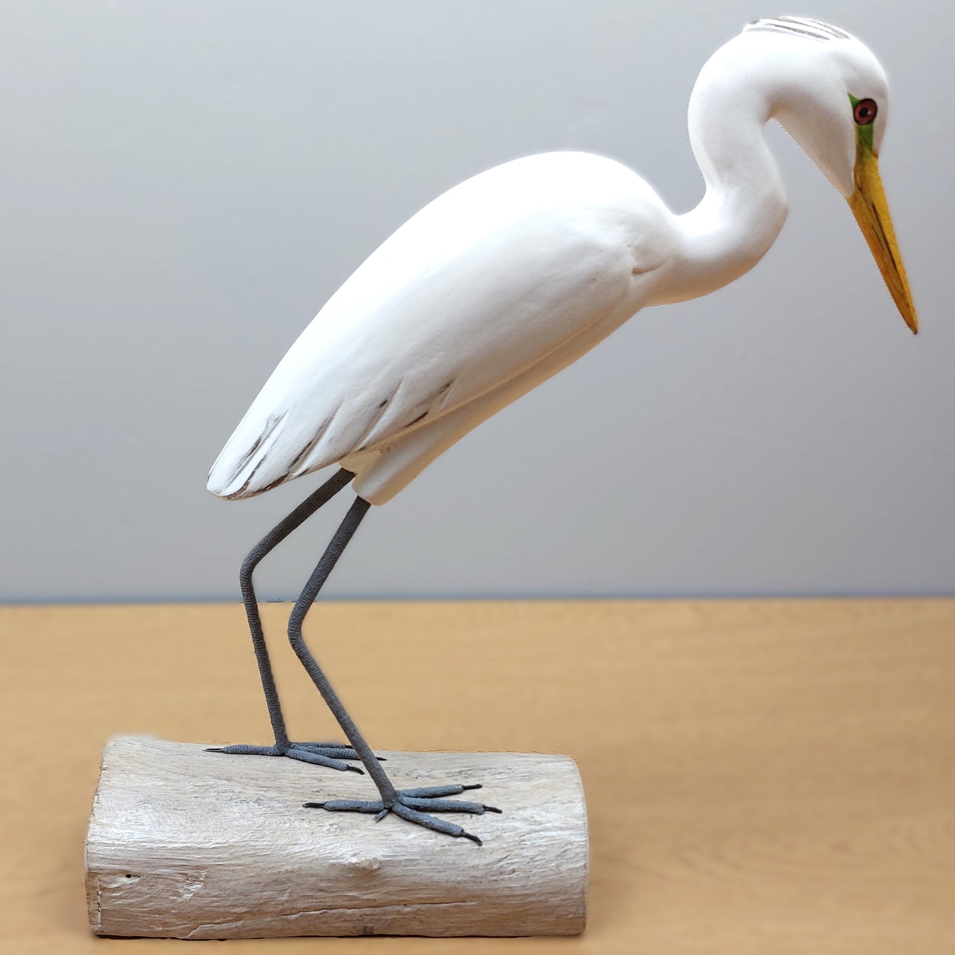 White hand carved Egret bird figurine on a wooden base against a plain background