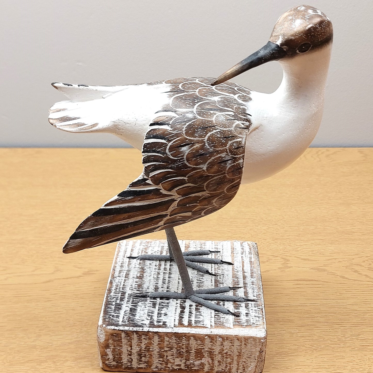 A hand carved and painted wooden Godwit Bird figurine, mounted on a wooden black against a wooden and pale background.