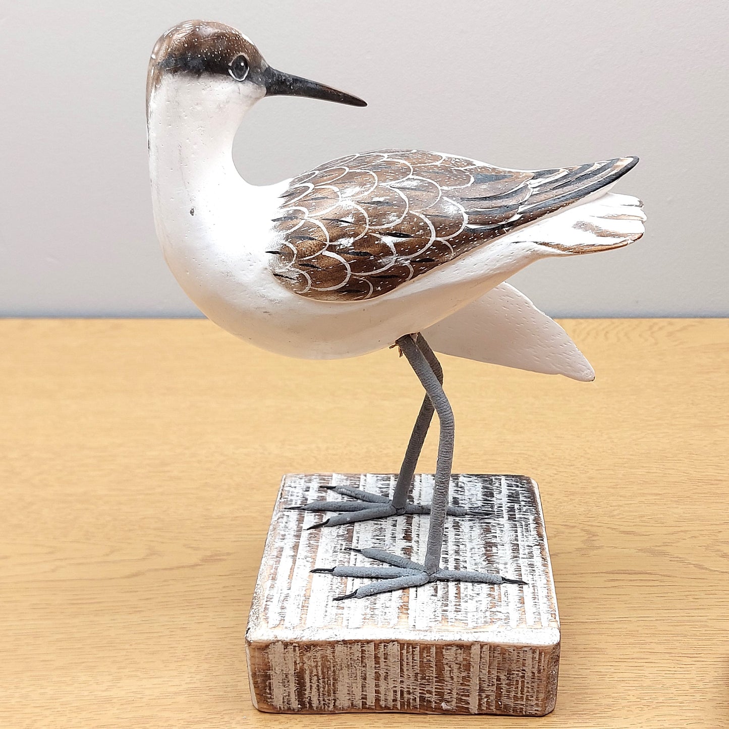 A hand carved and painted wooden Godwit figurine, looking backwards, mounted on a white painted wooden block.