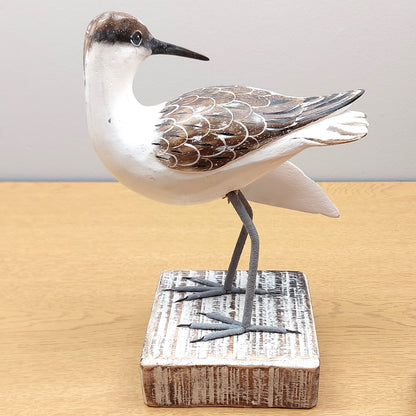 A hand carved and painted wooden Godwit figurine, looking backwards, mounted on a white painted wooden block.