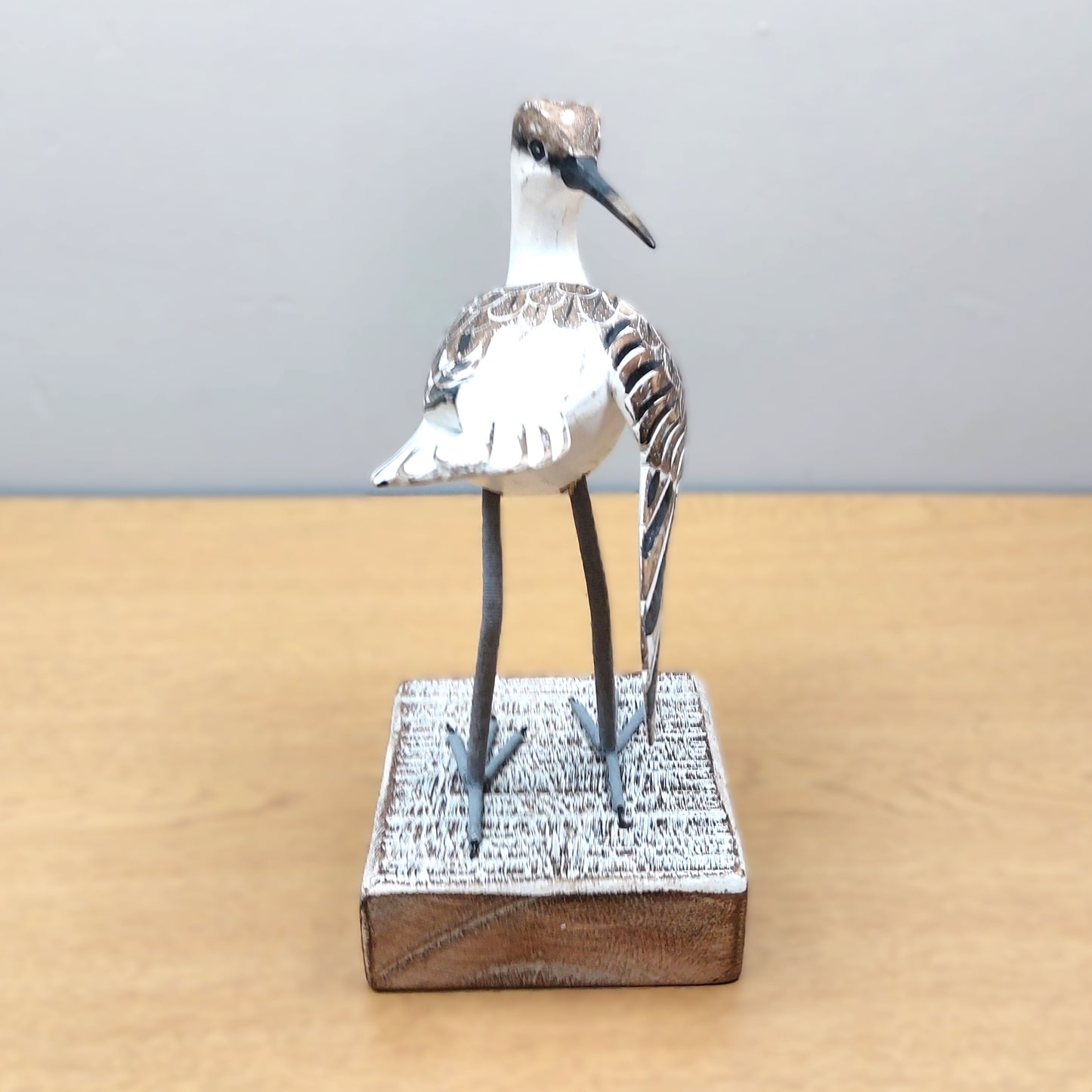 Wooden Model of an ornate Godwit bird on a whitewashed wooden base on a beige surface.