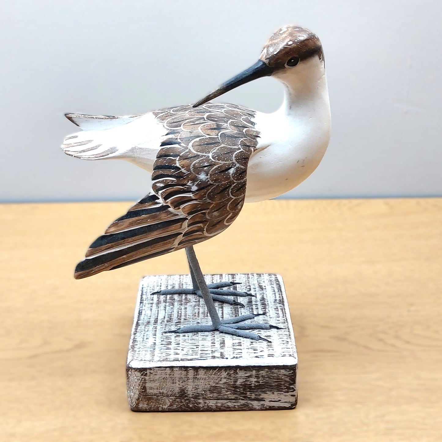 Wooden carved and hand painted Godwit bird figurine on a stand with a plain background