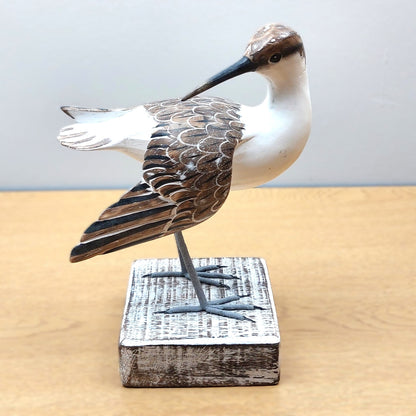 Wooden carved and hand painted Godwit bird figurine on a stand with a plain background