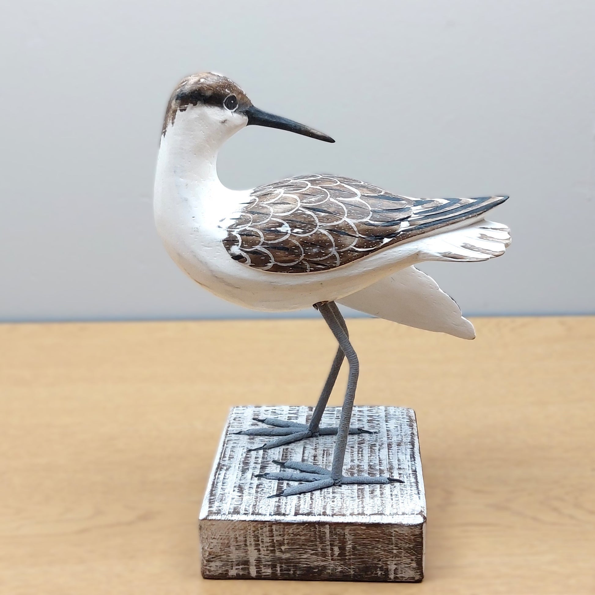 Decorative white and brown carved wooden Godwit bird figurine on a wooden base against a plain background