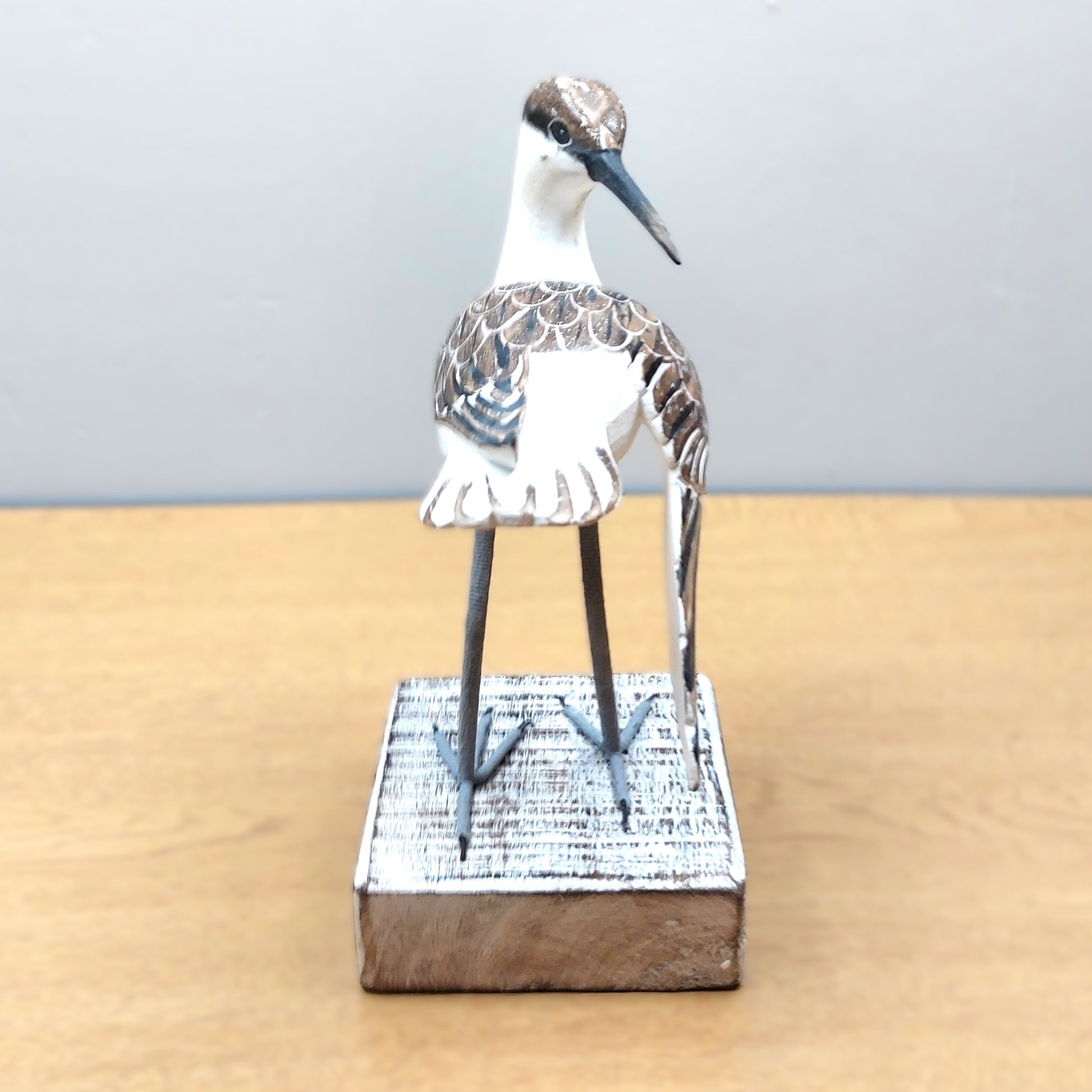 Decorative ornate hand made and painted Godwit bird figurine on a wooden base against a plain background