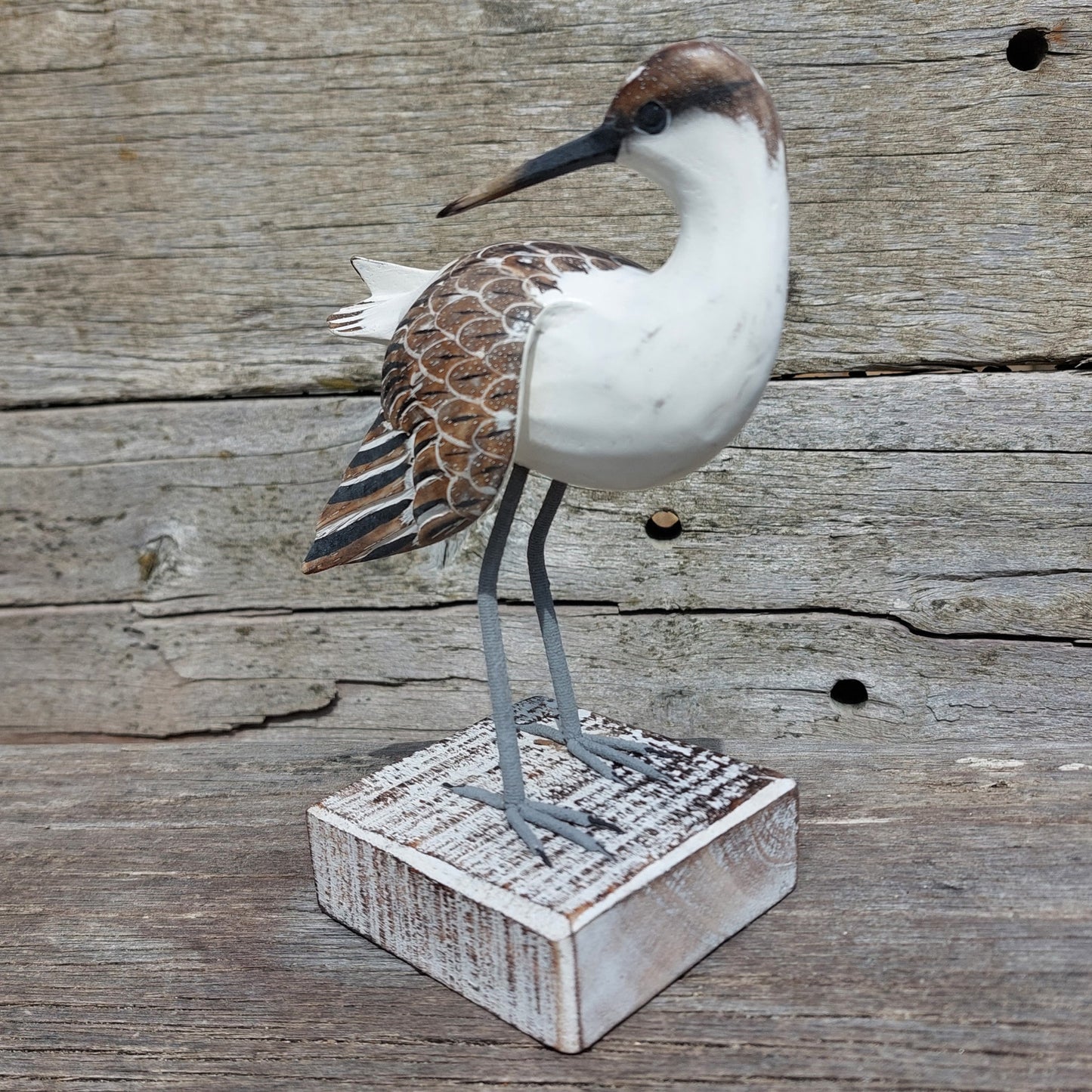 Decorative hand carved and painted wooden Godwit bird figure on a wooden base against a rustic wooden background