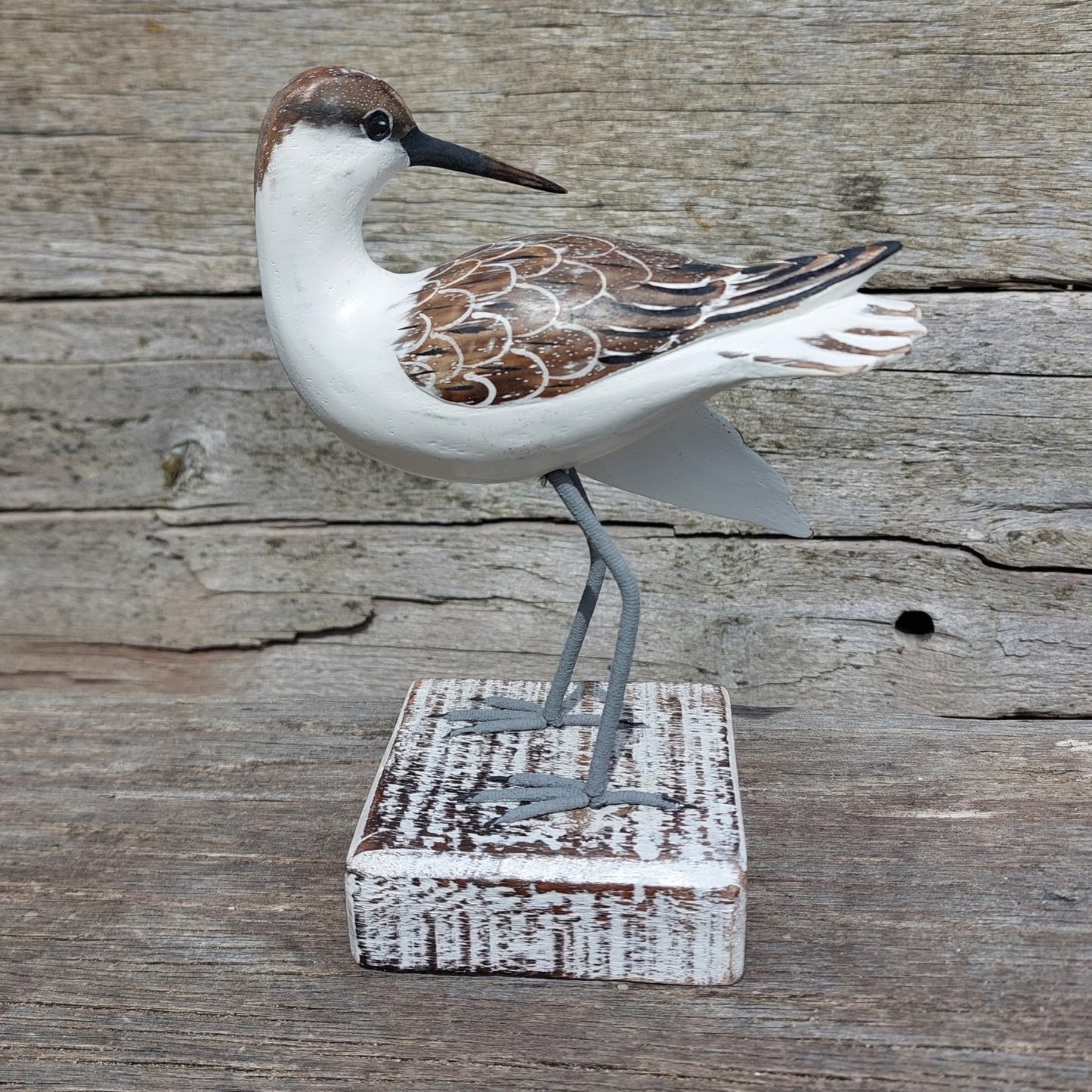 Decorative handmade and painted Godwit bird sculpture on a wooden block against a rustic wooden background