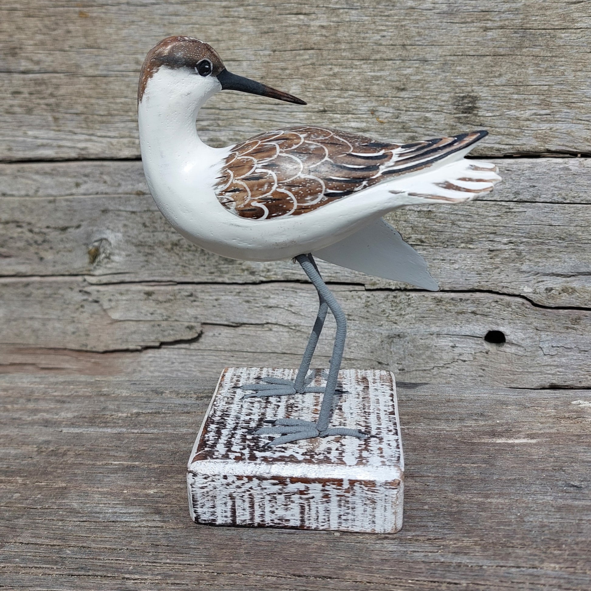 Decorative handmade and painted Godwit bird sculpture on a wooden block against a rustic wooden background