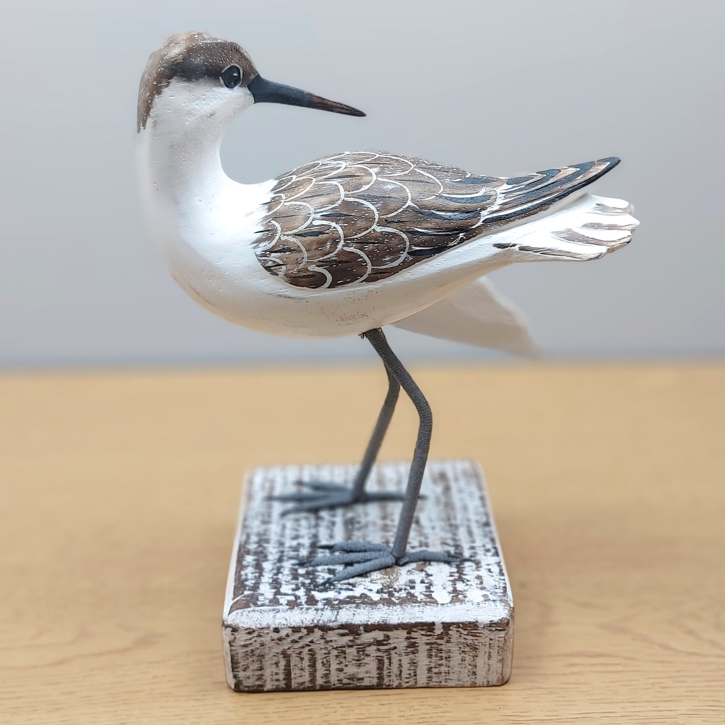 Decorative Godwit bird sculpture on a wooden base with a plain background