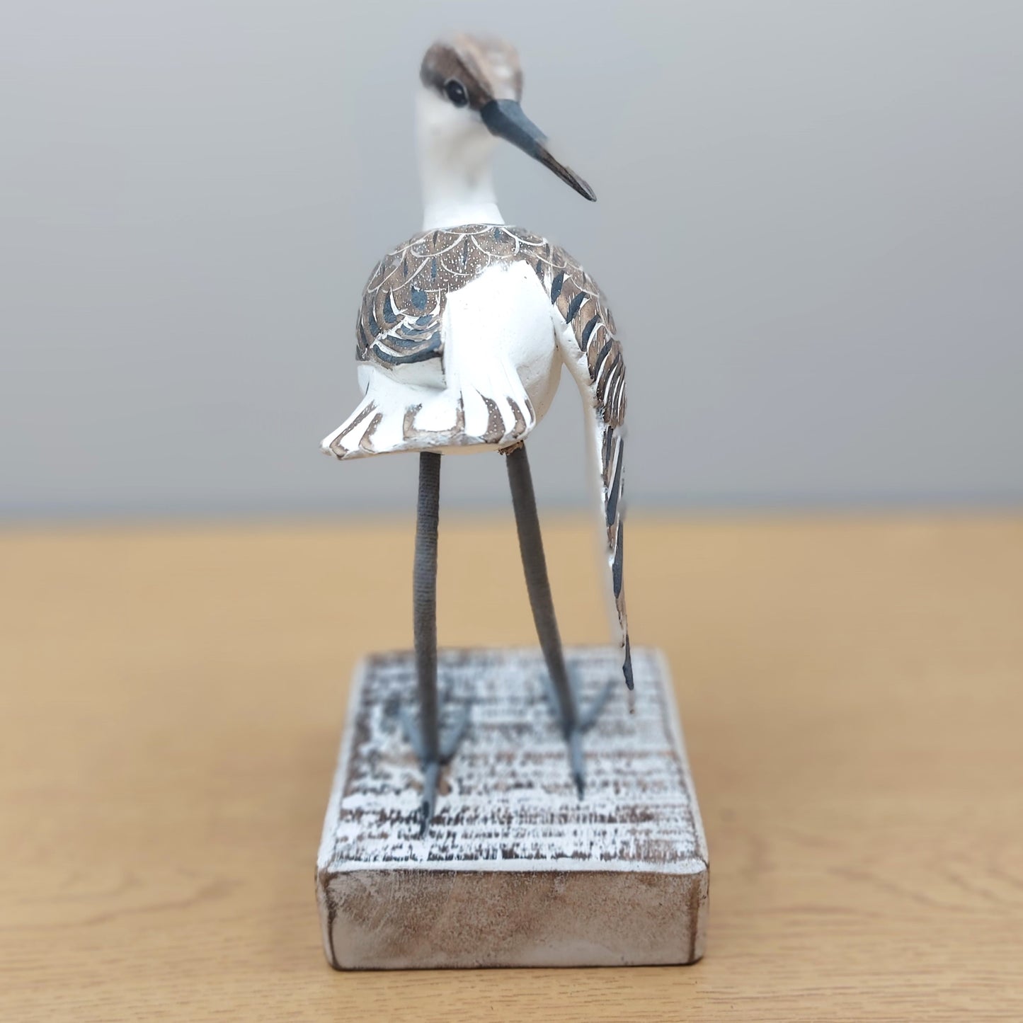 Straight on angle of a decorative Godwit bird figurine on a wooden base with a plain background