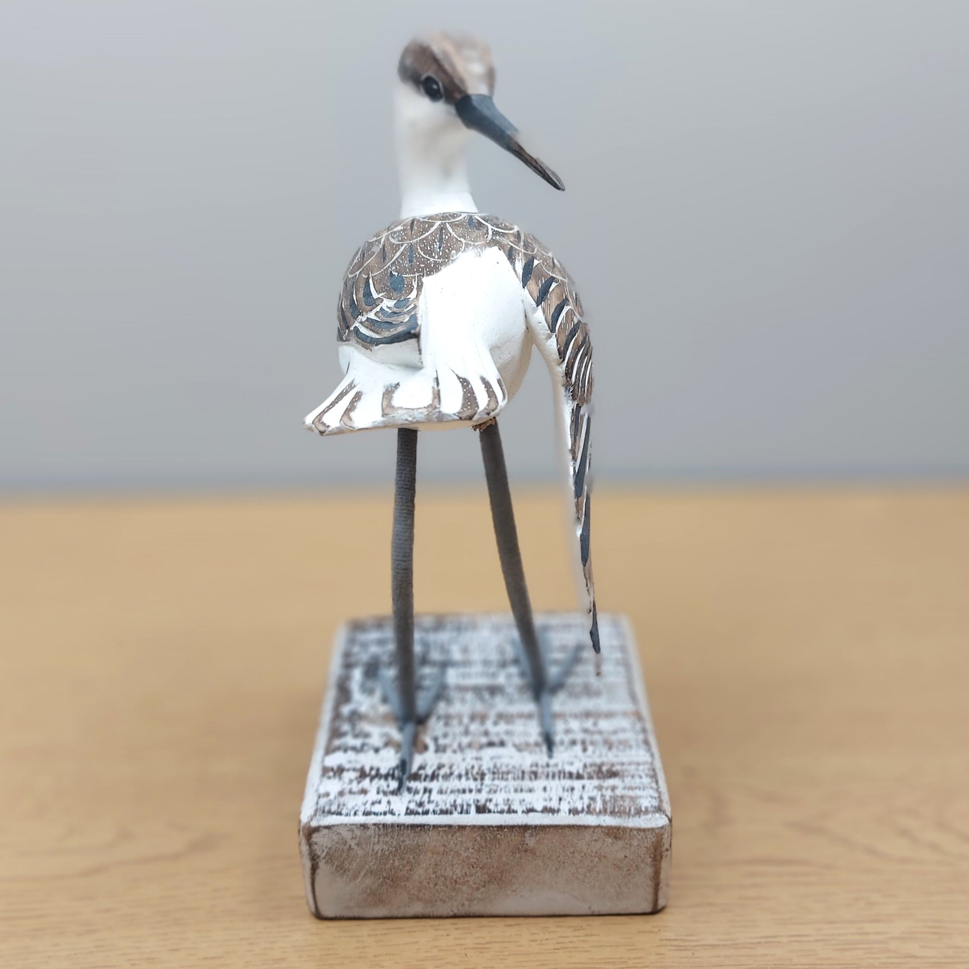 Straight on angle of a decorative Godwit bird figurine on a wooden base with a plain background