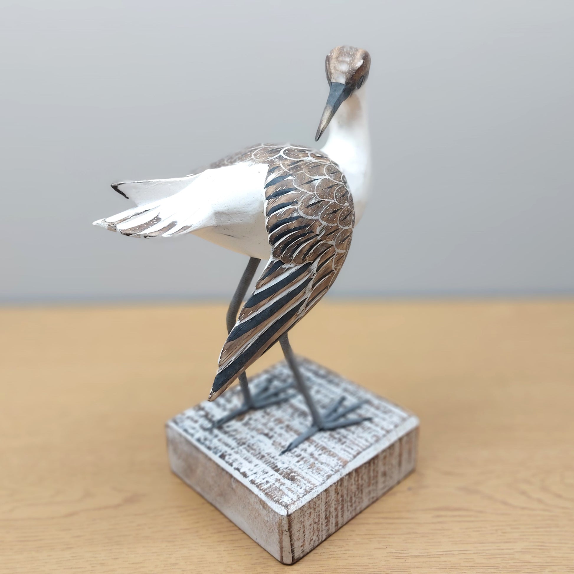 Decorative hand carved and painted Godwit bird figurine on a wooden base against a plain background