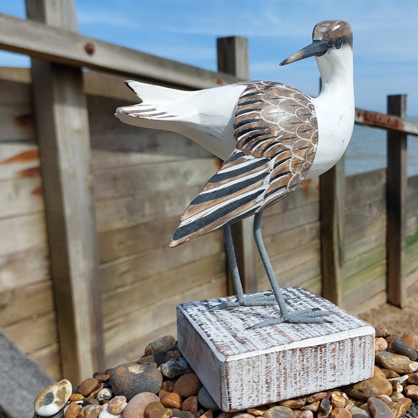 Decorative Wooden Godwit bird sculpture on a wooden base with a beach background
