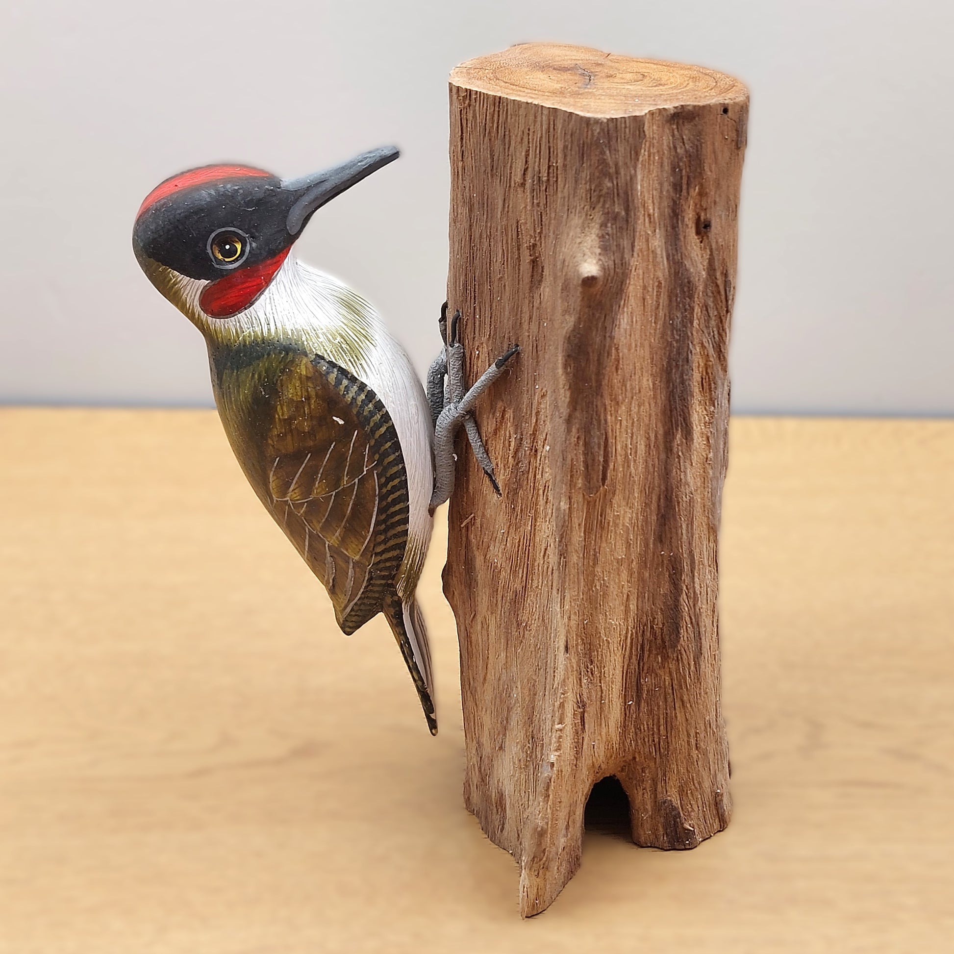 Hand carved and painted Woodpecker figurine mounted on a wood log against a plain background