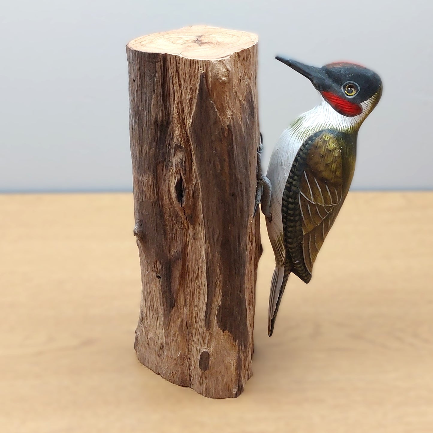 Hand carved and painted wooden Green Woodpecker figurine mounted against a wood log on a pale background