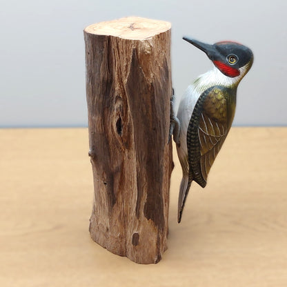 Hand carved and painted wooden Green Woodpecker figurine mounted against a wood log on a pale background