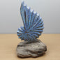 Decorative hand carved and painted blue shell sculpture on a wooden base against a plain background